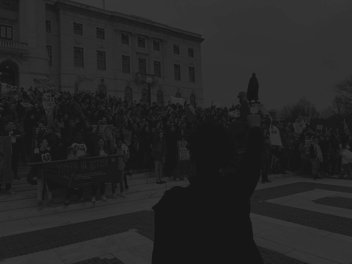 A crowd of youth in protest in front of the Rhode Island State House with fists in the air